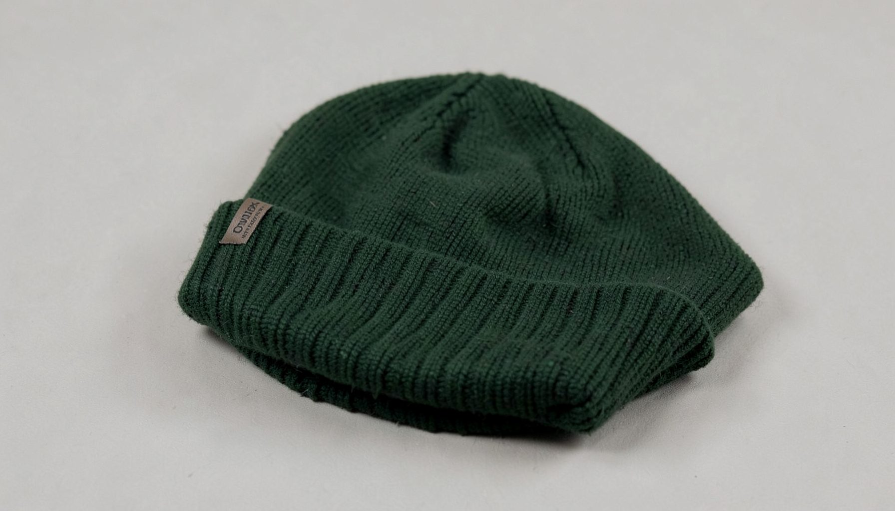 A knit beanie in hunter green resting on a neutral surface, soft folds visible