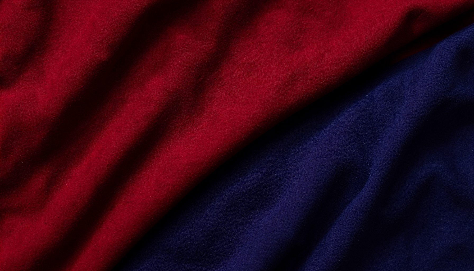 Deep crimson red and navy blue textured streetwear backdrop with soft folded fabric shadows, moody and bold