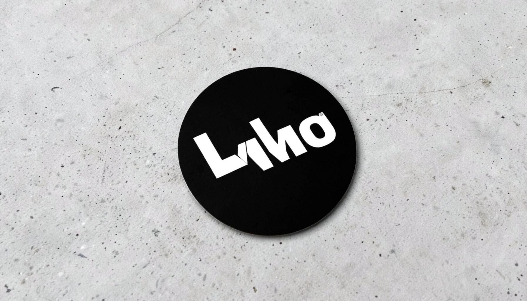 A black circular sticker with bold white lettering, placed diagonally on a light concrete background