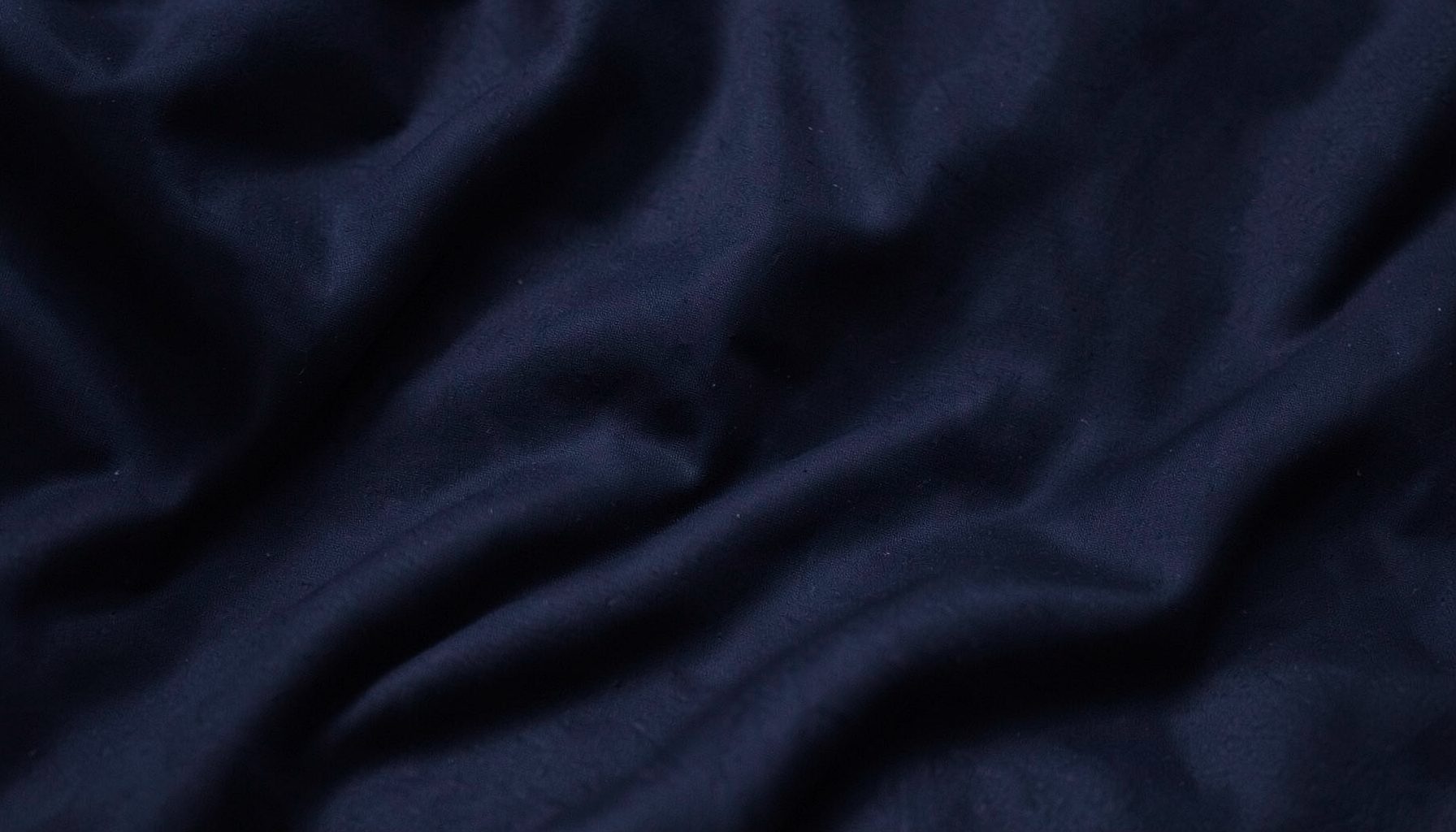 Dark textured fabric backdrop with soft folds, deep navy and charcoal tones, moody and understated streetwear atmosphere