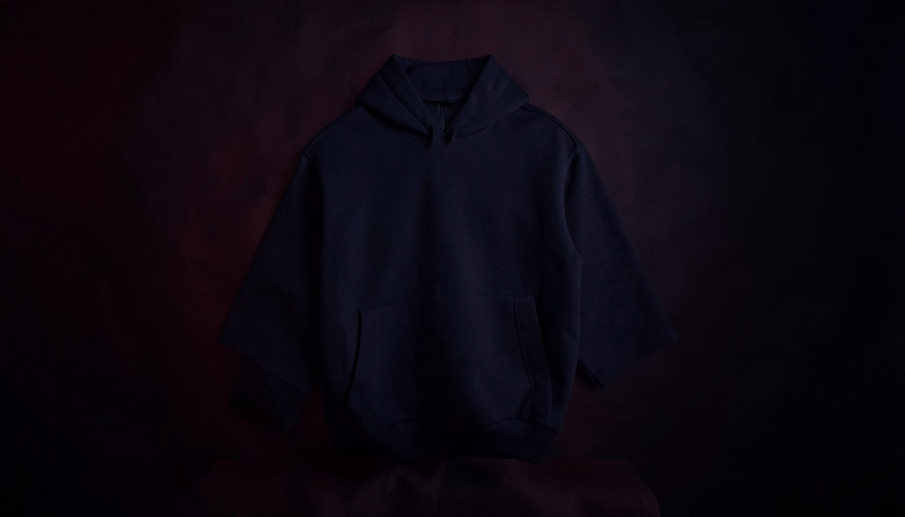 Dark moody backdrop with soft crimson and navy tones, evoking a streetwear brand atmosphere