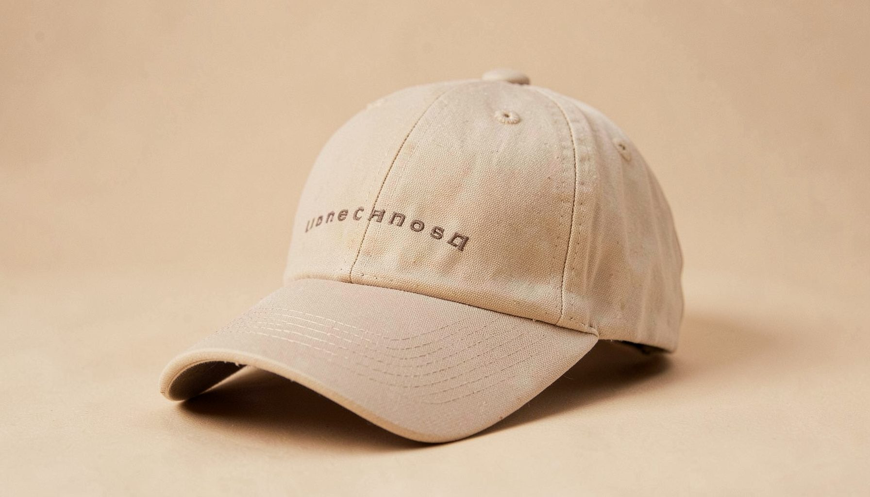 A beige baseball cap with understated branding, set against a warm neutral backdrop