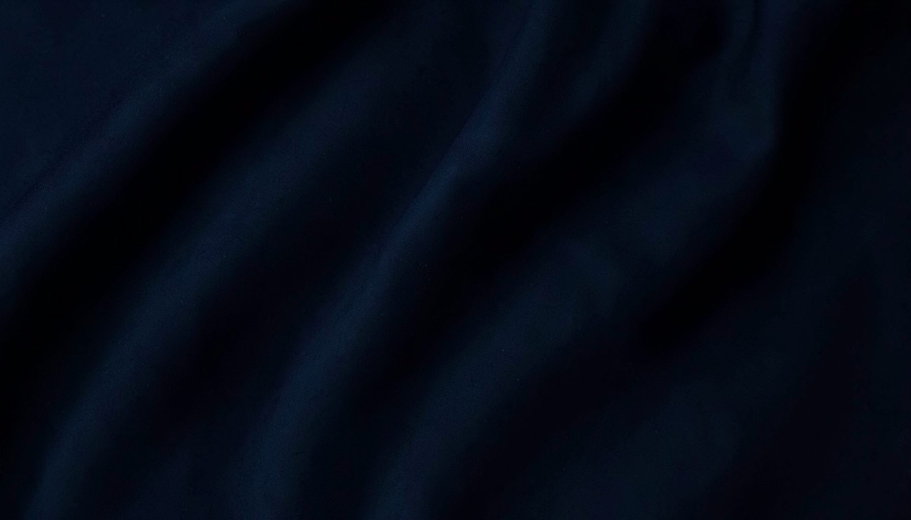 Dark moody backdrop with deep navy and charcoal tones, soft folded fabric shadows