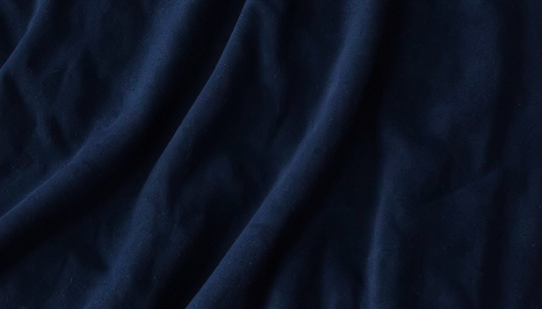 Dark textured fabric backdrop with soft folds, deep navy and charcoal tones, moody and understated streetwear atmosphere